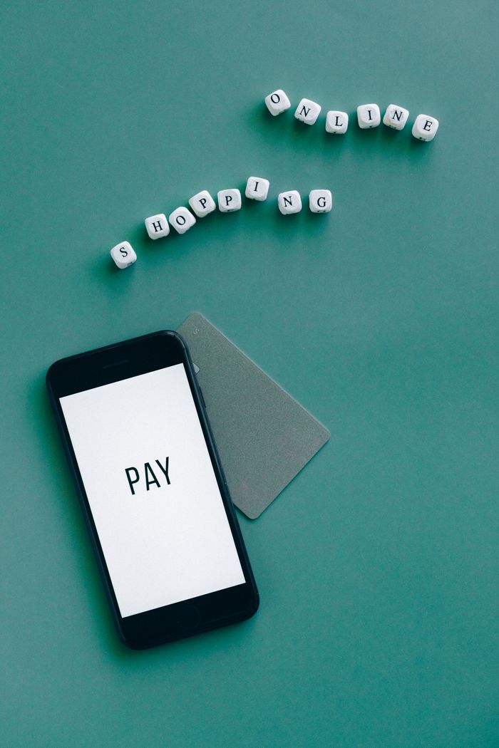 Smartphone with the word 'Pay' displayed alongside a card and letters spelling 'Shopping Online' on a green background.